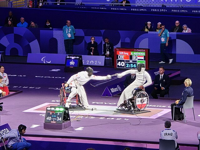 Two people in wheelchairs, fencing 