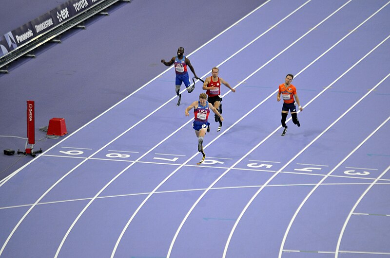 Hunter Woodhall, a white man who uses two prosthetic legs, crossing the finish line on a purple track